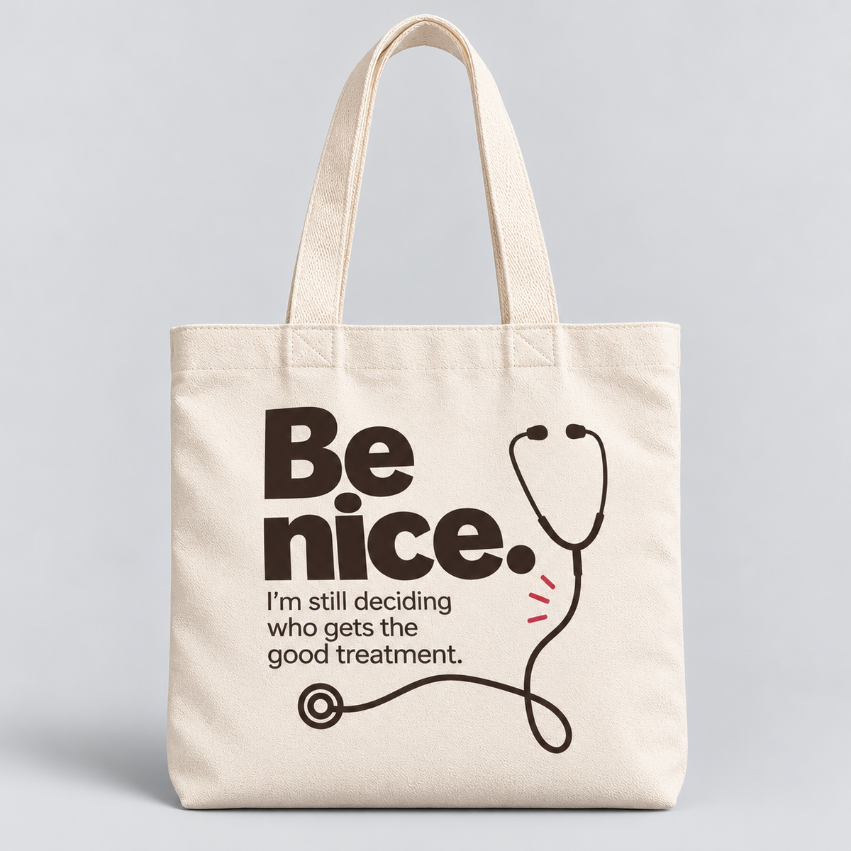 Male healthcare professional in sage-green scrubs carrying a cream tote bag printed with “Be nice. I’m still deciding who gets the good treatment” and a black stethoscope illustration.